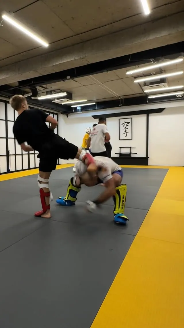 Full-contact kumite during the camp — one athlete throwing a high kick, both in shin guards